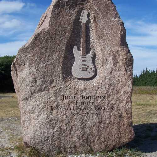 Rund 2,5 m hoher Gedenkstein aus rotem Granit, der an der Stelle der ehemaligen Bühne steht und an Das Love-and-Peace-Festival und Jimi Hendrix' letzten Festival-Auftritt erinnert.<br/>
 («Jimi Hendrix – Fehmarn – Love and Peace Festival» Sept. 1970»).