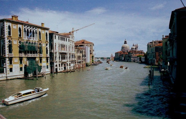 Grand Canal in Venice, Italy where boat taxis pass by marble palaces of medieval merchants with view of Santa Maria de la Salute Church, built to commemorate the end of the black death epidemic.