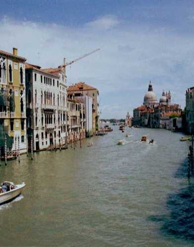 Grand Canal in Venice, Italy where boat taxis pass by marble palaces of medieval merchants with view of Santa Maria de la Salute Church, built to commemorate the end of the black death epidemic.