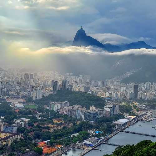 The Christ the Redeemer statue on top of dramatic Corcovado mountain shrouded by clouds, whose beams of light shine onto the vibrant city scape of Rio de Janeiro, Brazil.